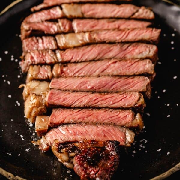 Sliced ribeye steak on black plate sprinkled with salt flakes.