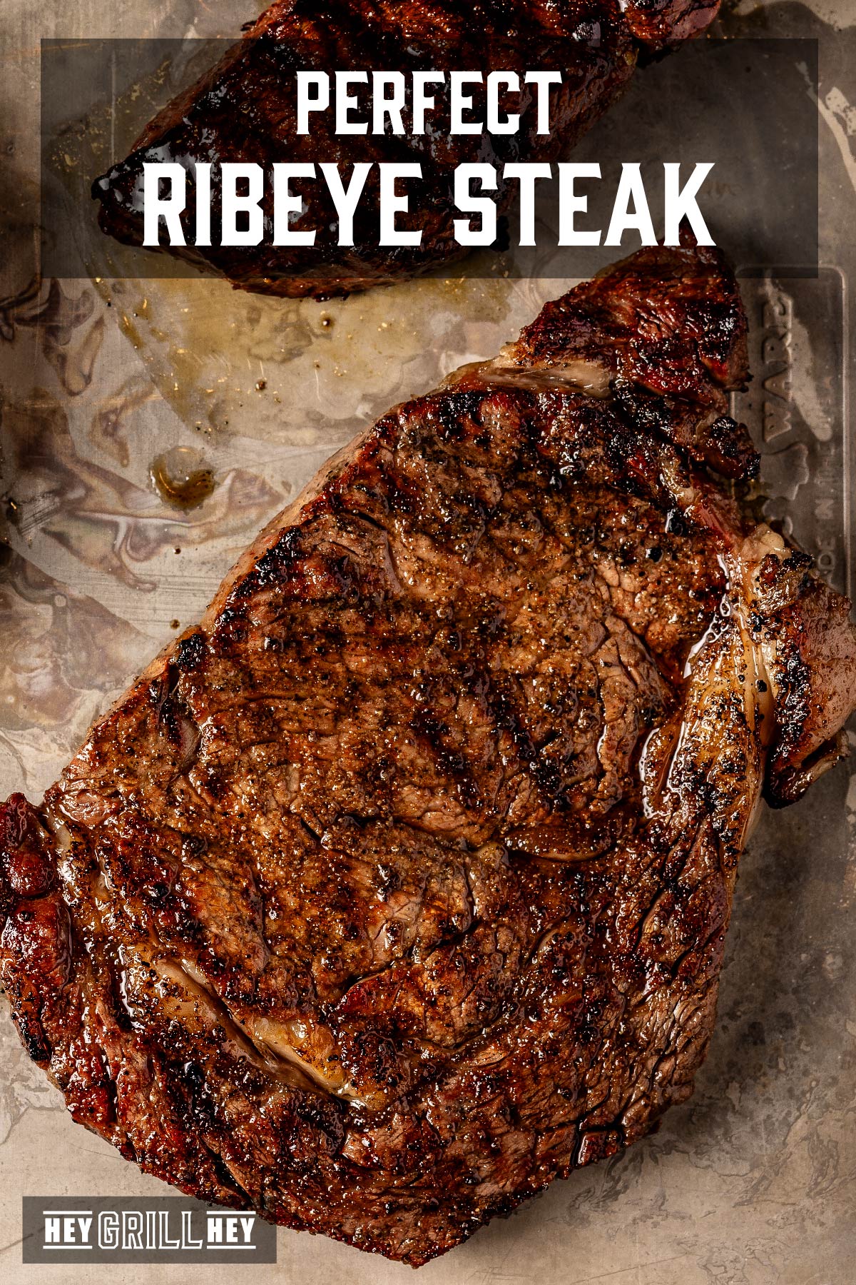 A grilled ribeye on a metal pan.  The text is read "Perfect ribeye steak".