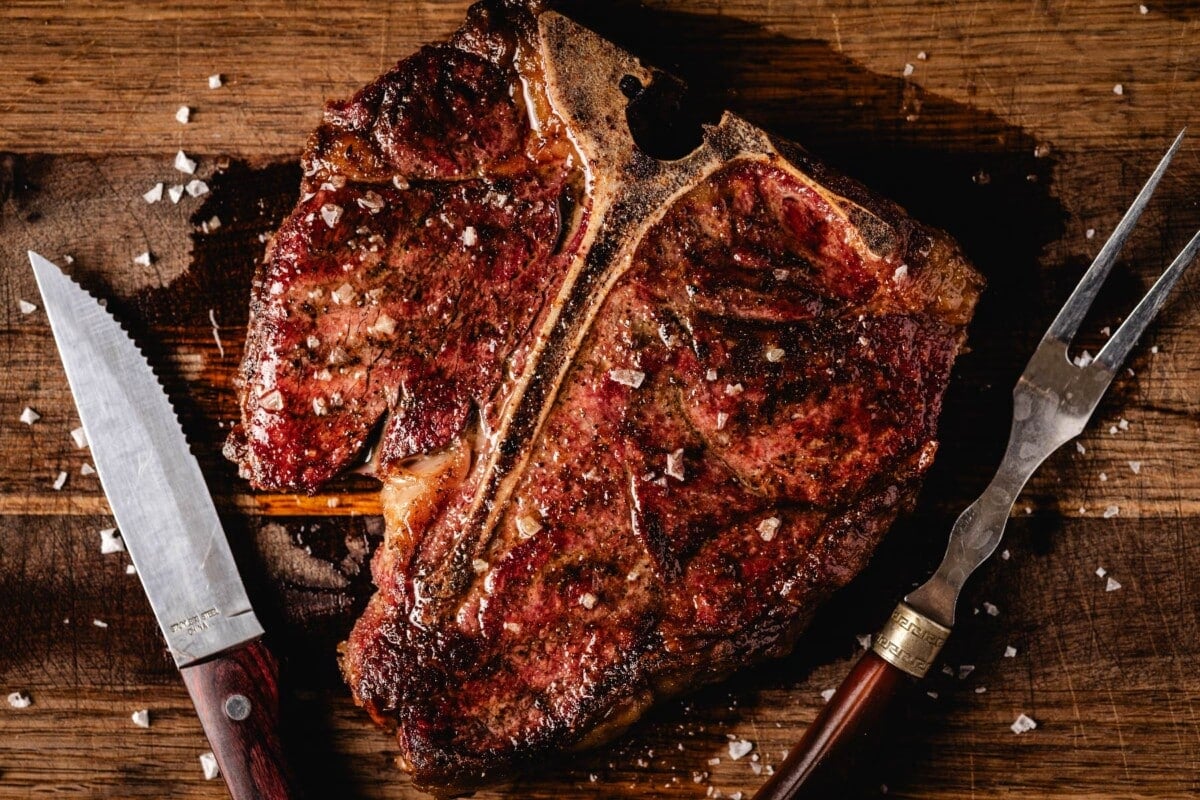 Grilled steak on cutting board next to knife and carving fork.