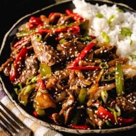 Pepper steak stir fry in bowl with rice, next to fork.