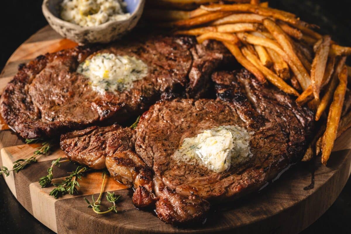 Steak frites on serving platter topped with mâitre d'hôtel butter, with a side of fries.