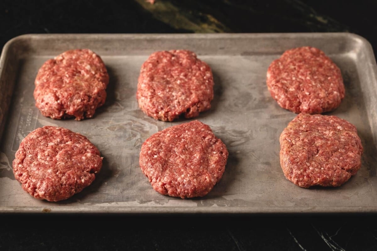 Steak patties on metal baking sheet.