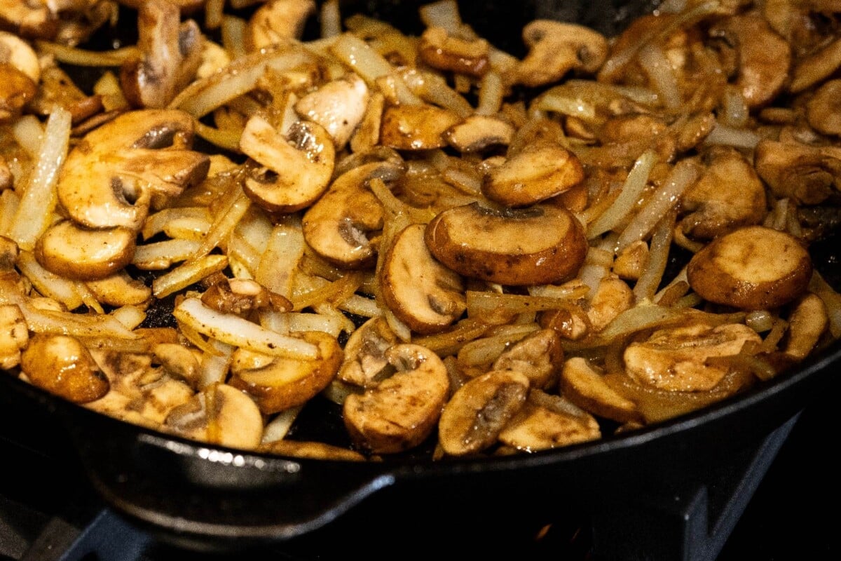Mushrooms and onions frying in cast iron skillet.