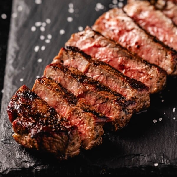 Sliced sirloin steak on black serving platter with salt flakes.
