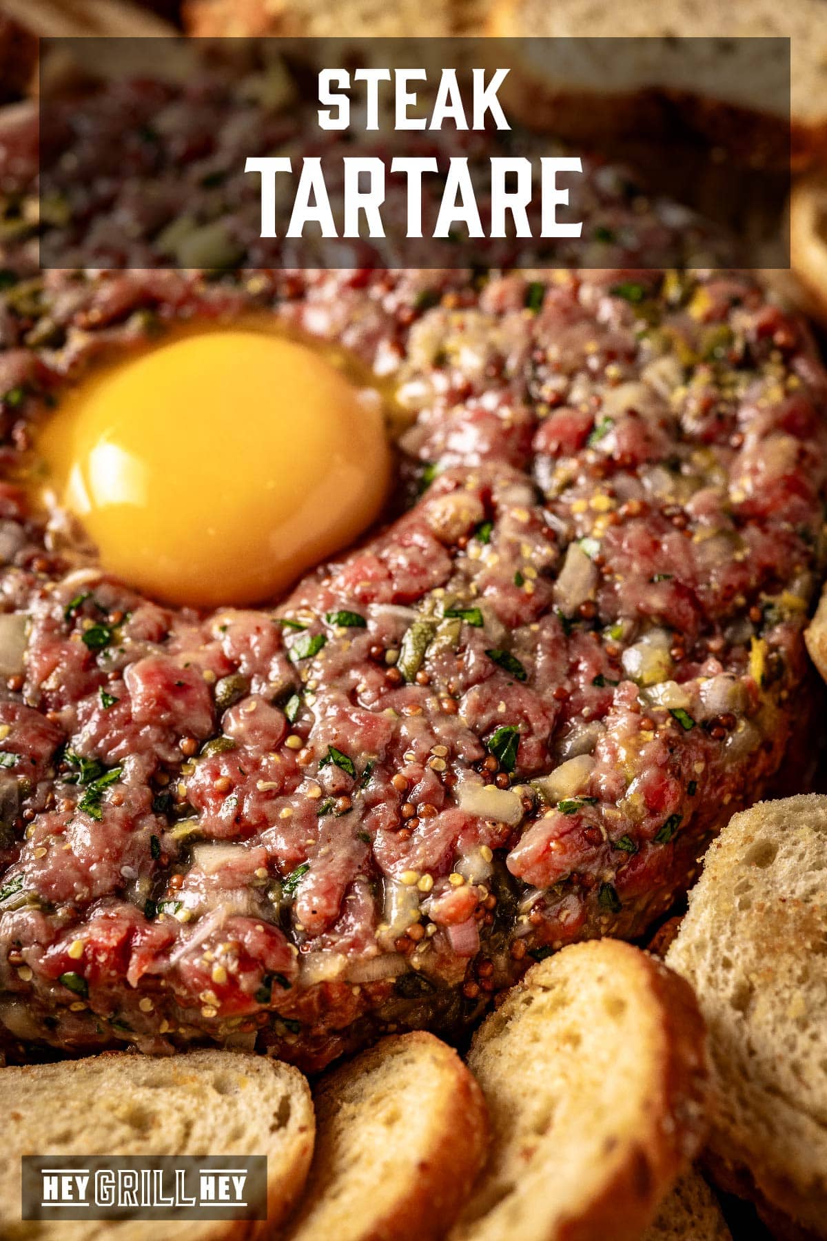 Steak tartare with egg yolk on top next to hard bread. Text reads "Steak Tartare".