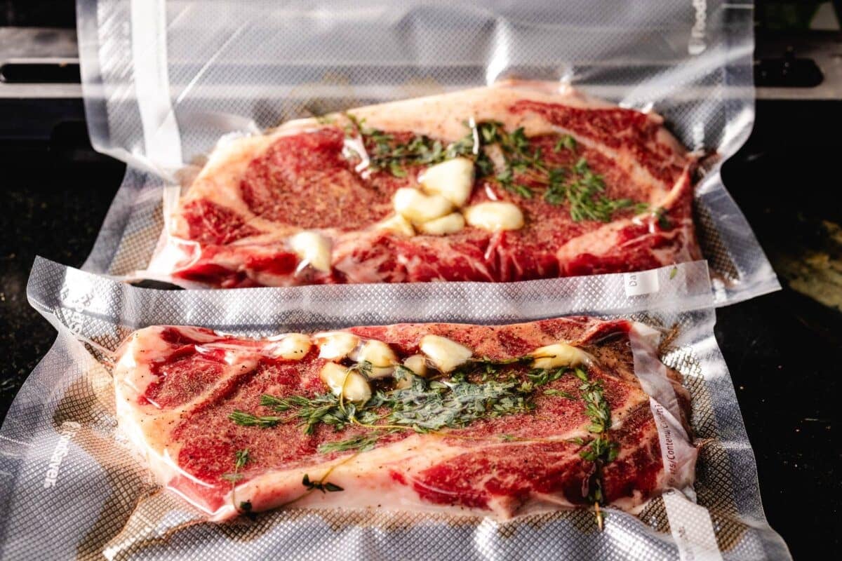 Ribeyes in sealed bags with garlic bulbs and springs of thyme.