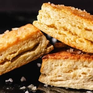 Homemade biscuits stacked on black surface.
