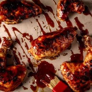 Chicken cuts on baking sheet drizzled with BBQ sauce.