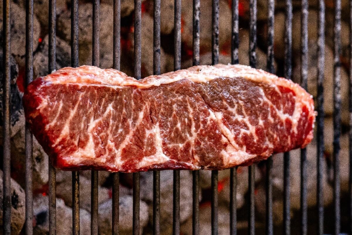 Raw sirloin on grill grates over indirect heat.