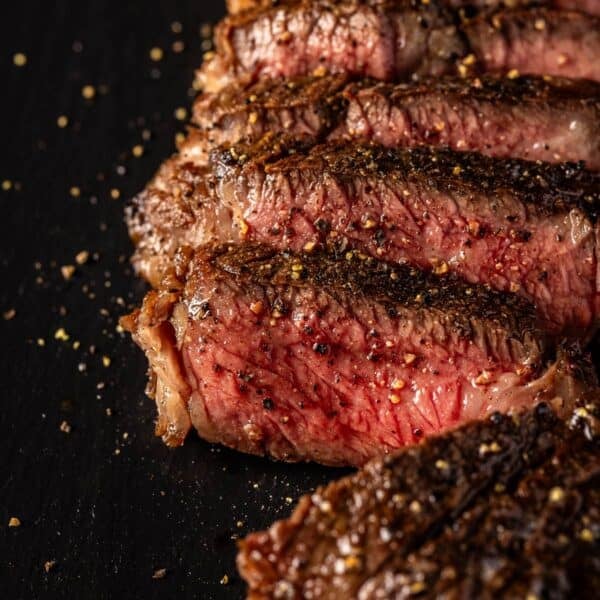 Sliced Denver steak on black cutting board sprinkled with flaky salt.