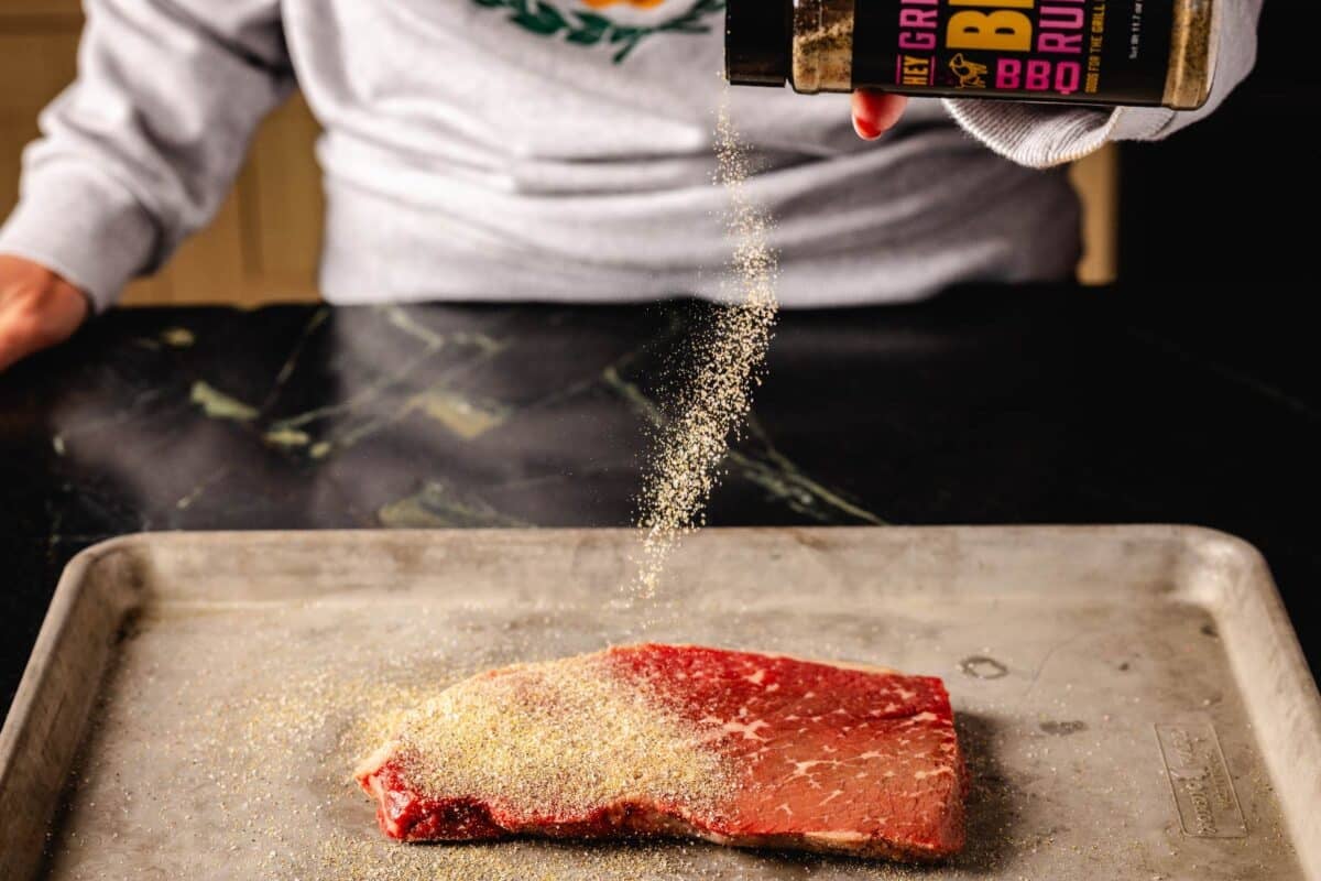 Steak on baking sheet being seasoned with Beef Rub.