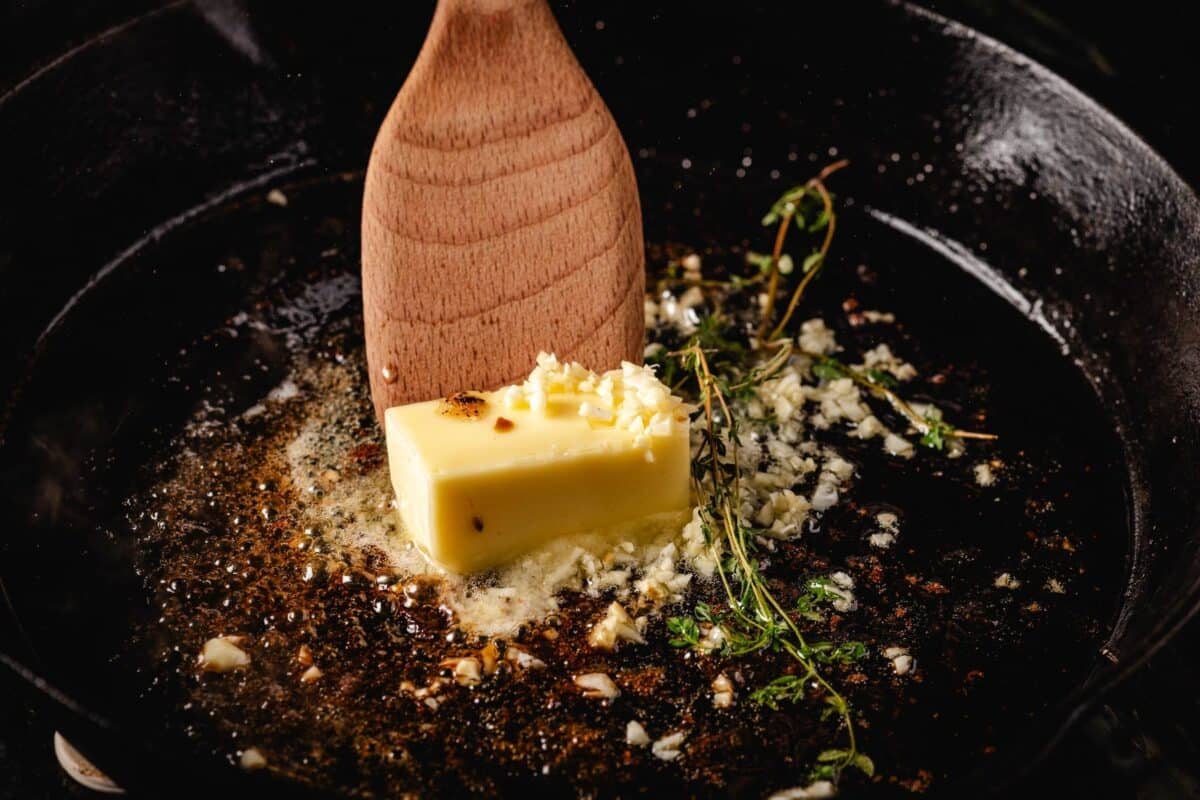 Wooden spoon stirring butter and herbs in skillet.