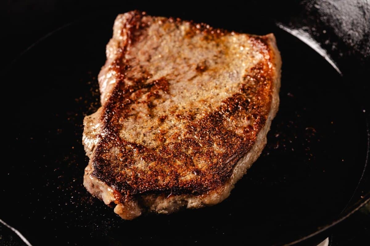 Steak grilling in cast iron skillet.