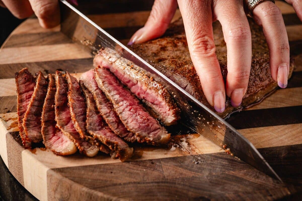 Knife slicing top round on cutting board.