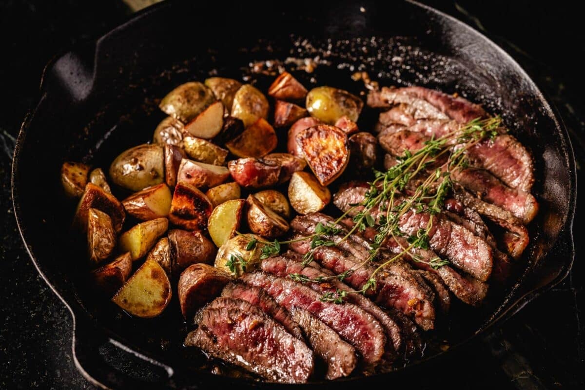 Sliced beed in skillet with potatoes and thyme sprig.