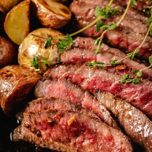 Sliced steak with potatoes in skillet.