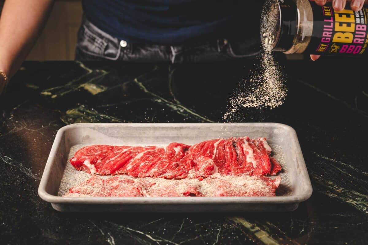 Flap steak on baking sheet being seasoned with Beef Rub.