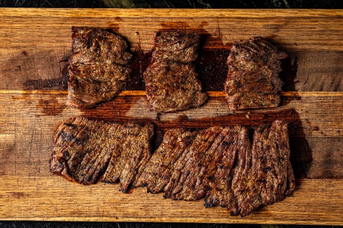 Grilled flap portions and full flap cut on wooden cutting board.