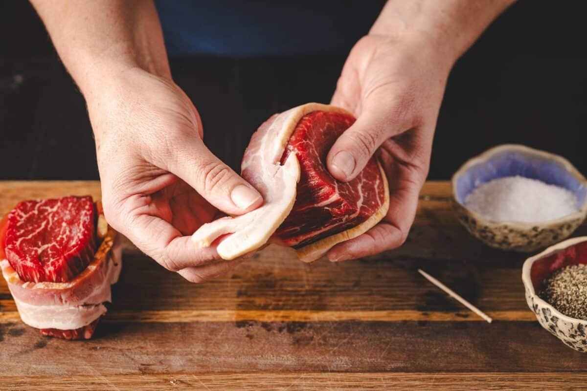 Filet being wrapped with bacon on wooden cutting board.