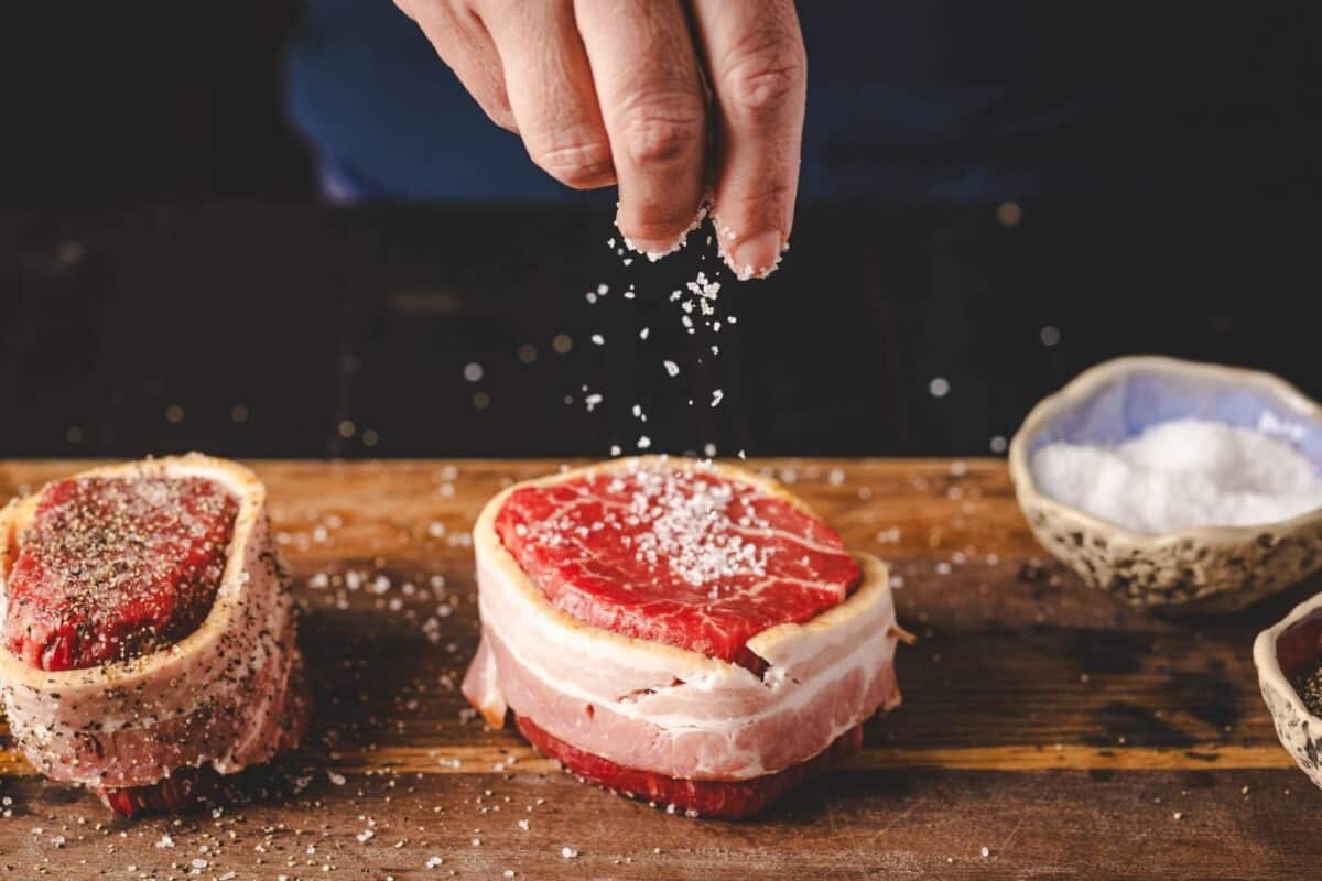 Bacon wrapped filet being sprinkled with salt.