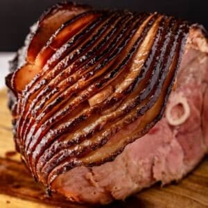 Sliced, glazed ham on wooden platter.