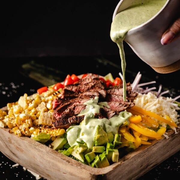 Steak salad ingredients in bowl being drizzled with jalapeño lime dressing.
