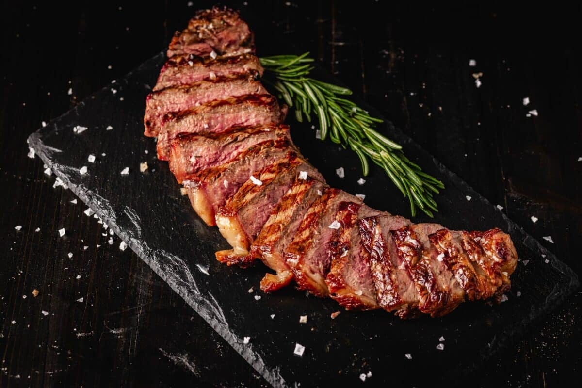 Sliced steak on serving platter with sprig of thyme.