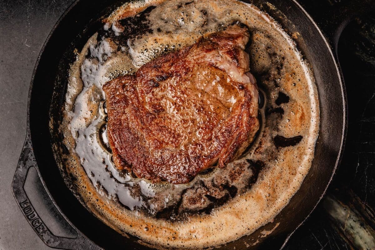 Ribeye searing in butter in cast iron skillet.