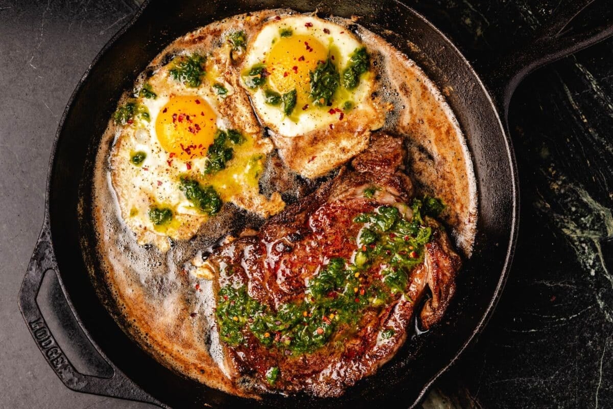 Seared ribeye in skillet with fried eggs.