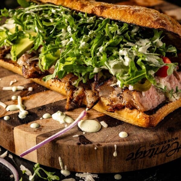 Steak sandwich with arugula and mayo on wooden platter.