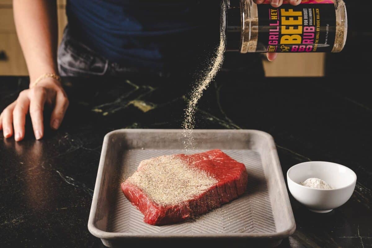 Beef roast on metal baking sheeting being seasoned with Beef Rub.