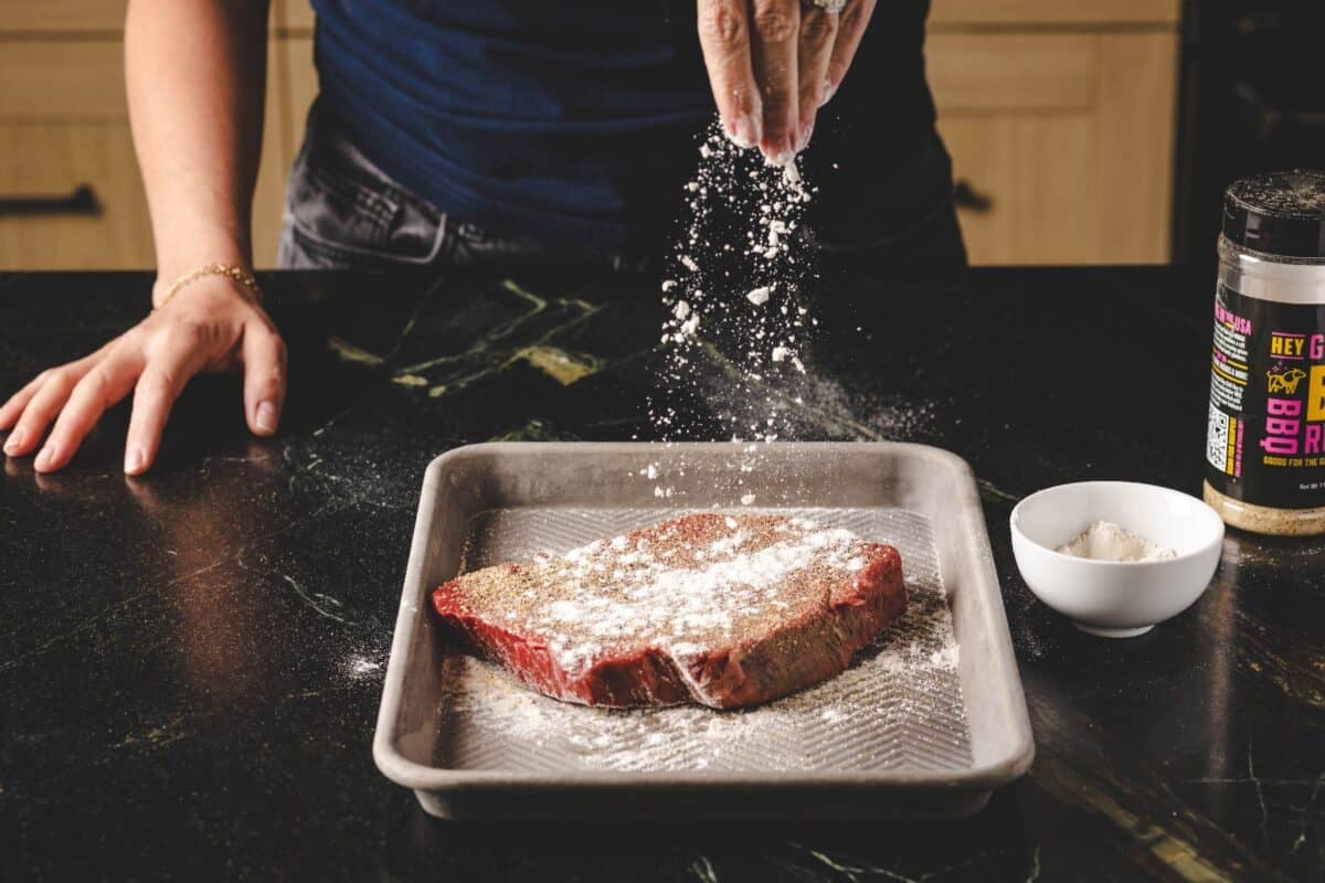 Beef roast on baking sheet being coated with flour.