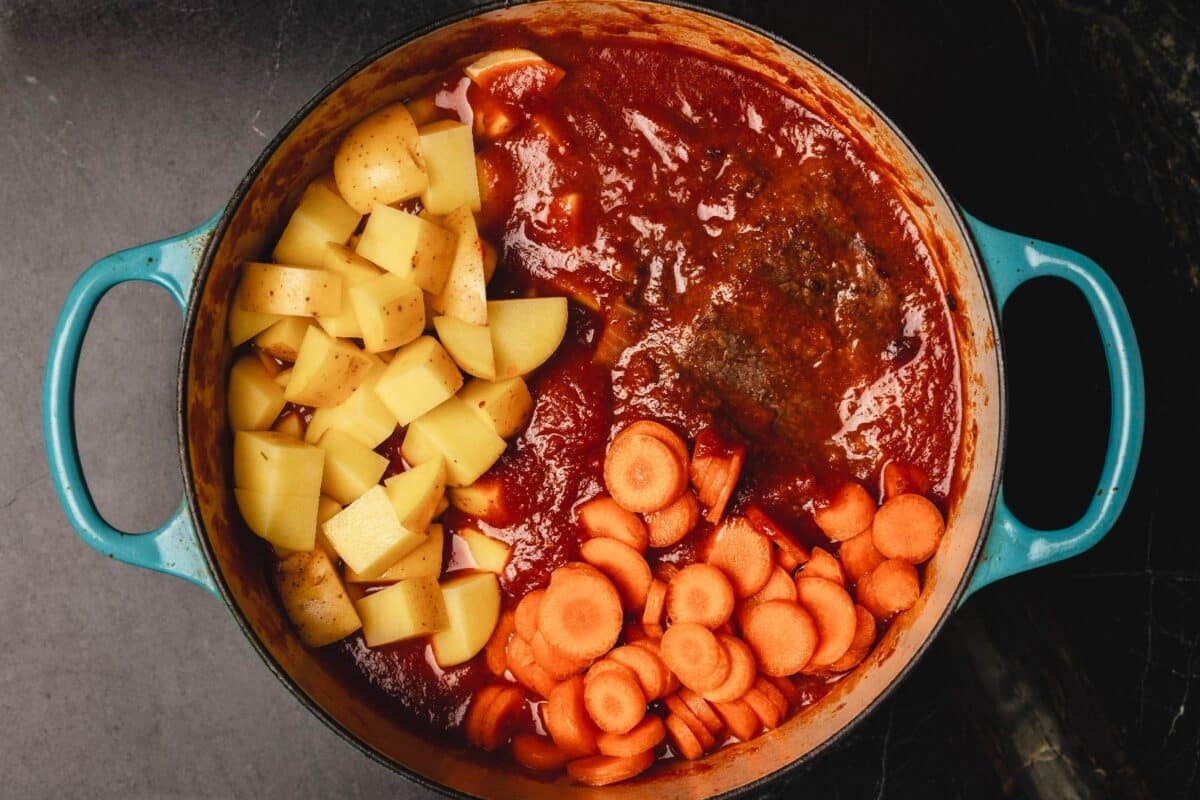 Diced potatoes and chopped carrots in tomato sauce in pot.