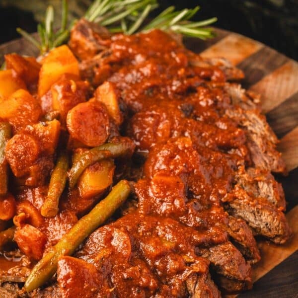 Seared steak smothered in tomato gravy, on a wooden platter next to thyme sprig.
