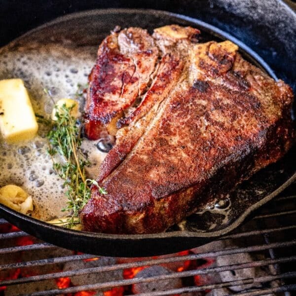 T-bone steak in skillet with butter pad and sprig of thyme.