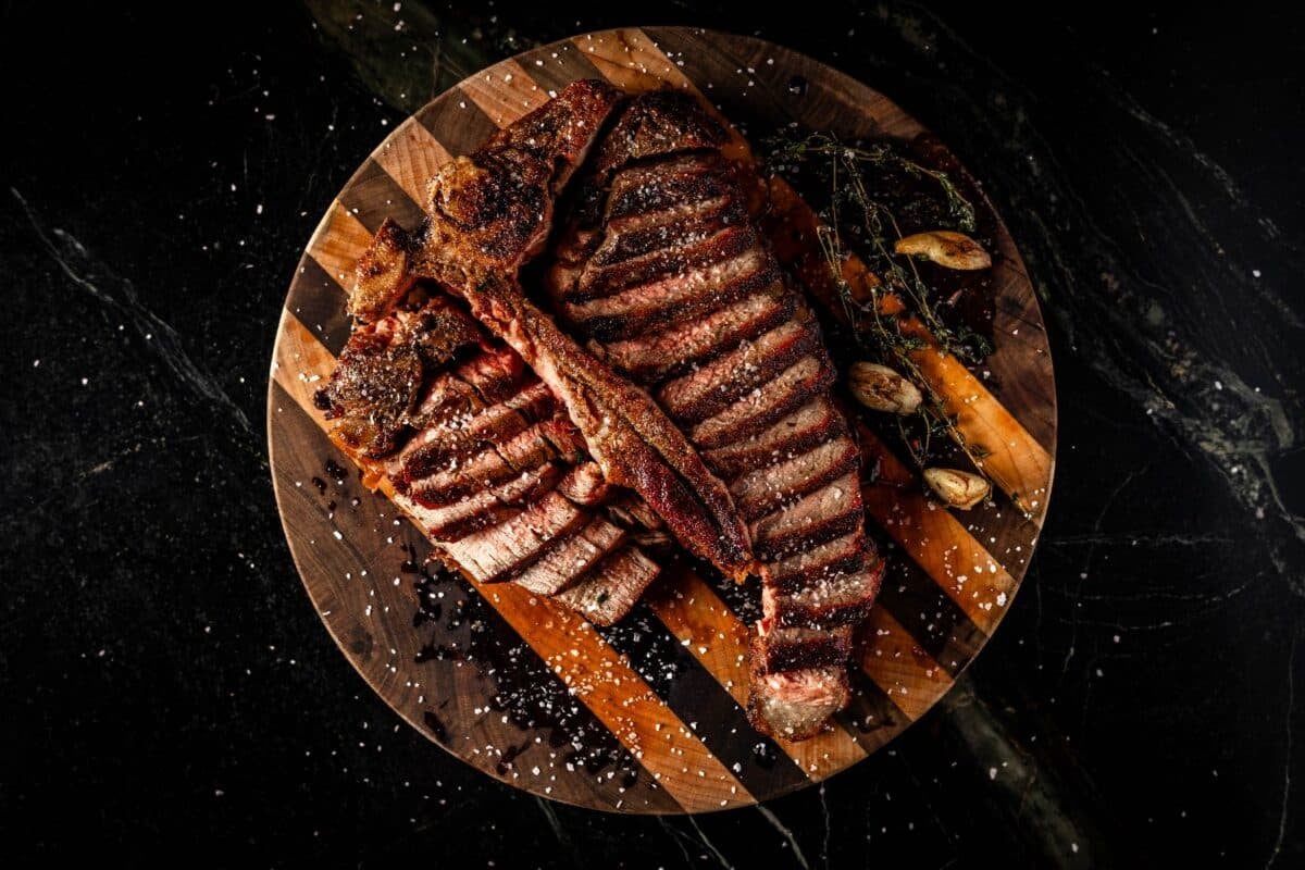 Sliced T-bone steak on wooden platter.