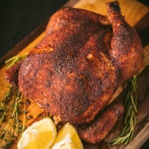 Smoked whole chicken on serving platter with lemon wedges.