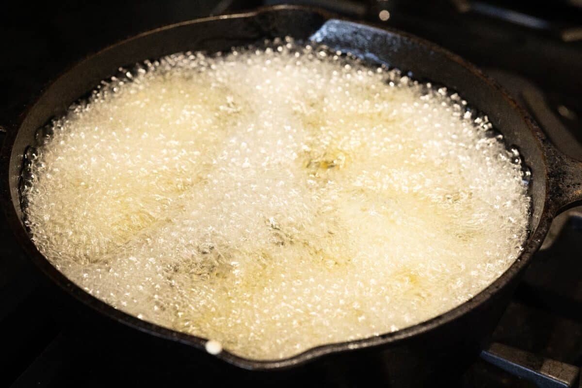 Battered fish filet frying in oil in cast iron pan.