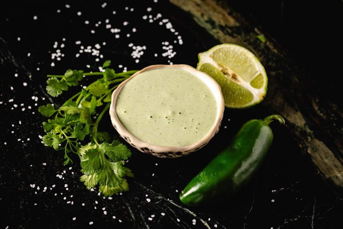 Sauce in bowl next to lime wedge, cilantro leaves, and a jalapeño.