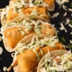 Fish tacos with toppings on black platter.