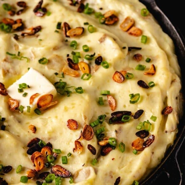 Mashed potatoes in skillet topped with butter and roasted garlic.
