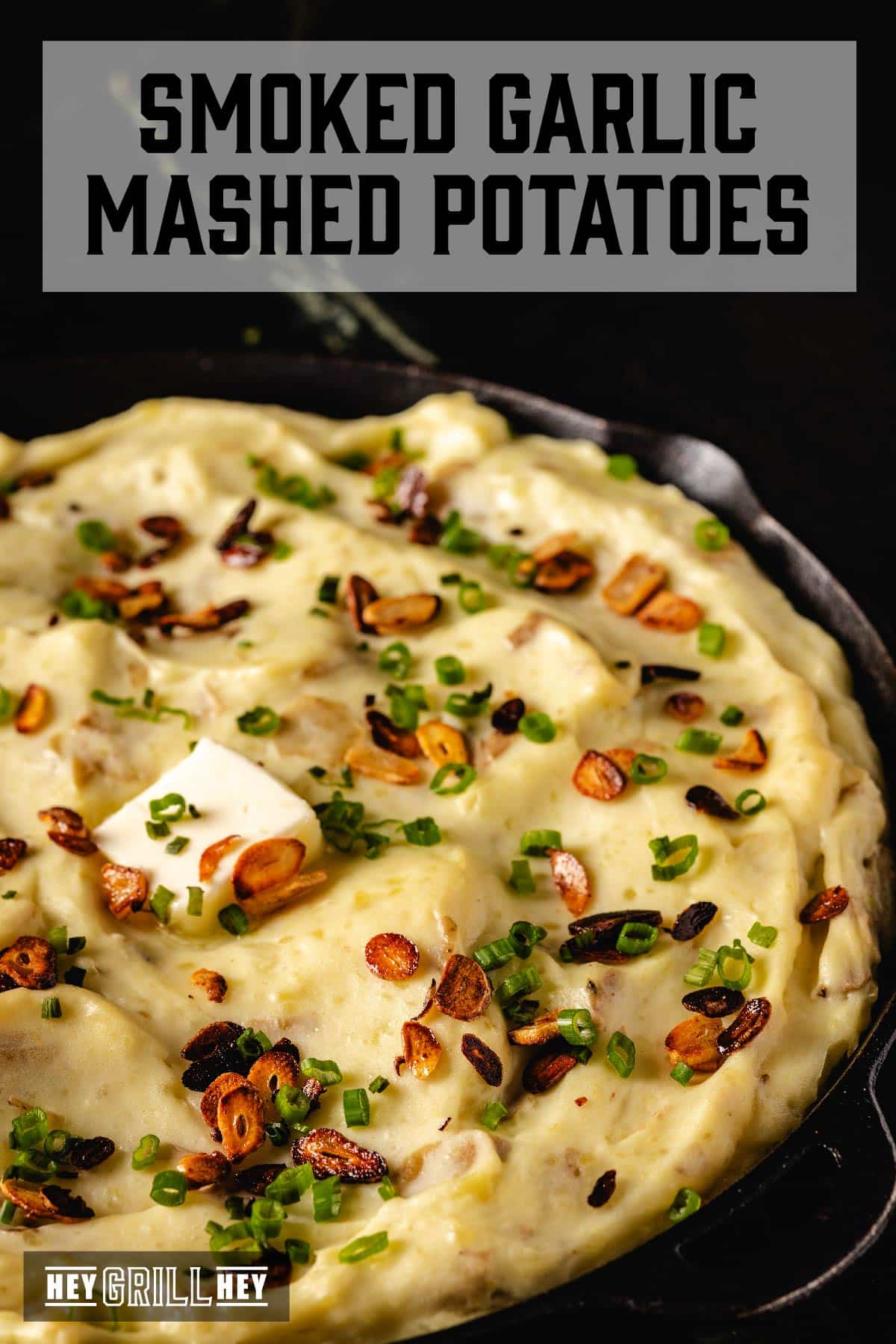 Mashed potatoes in skillet topped with butter and roasted garlic. Text reads "Smoked Garlic Mashed Potatoes".