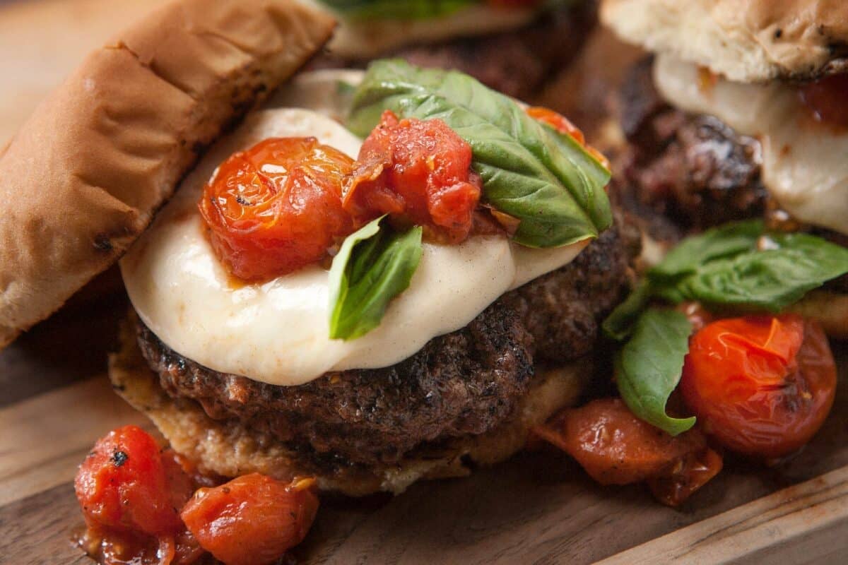 Close up of garlic butter burger topped with tomato and basil leaf.