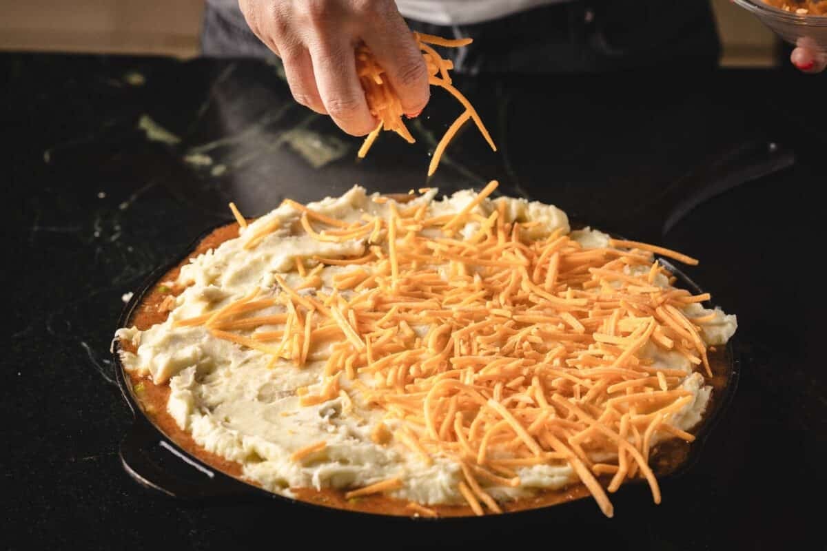 Shredded cheese being sprinkled onto mashed potato filling.