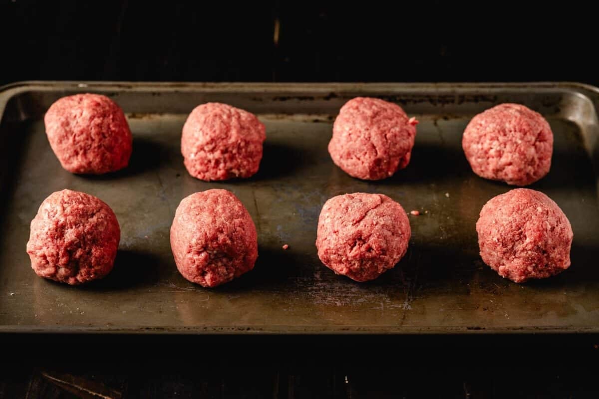 Balls of ground beef on metal baking sheet.