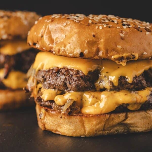Grilled cheeseburgers with sesame buns on black surface.