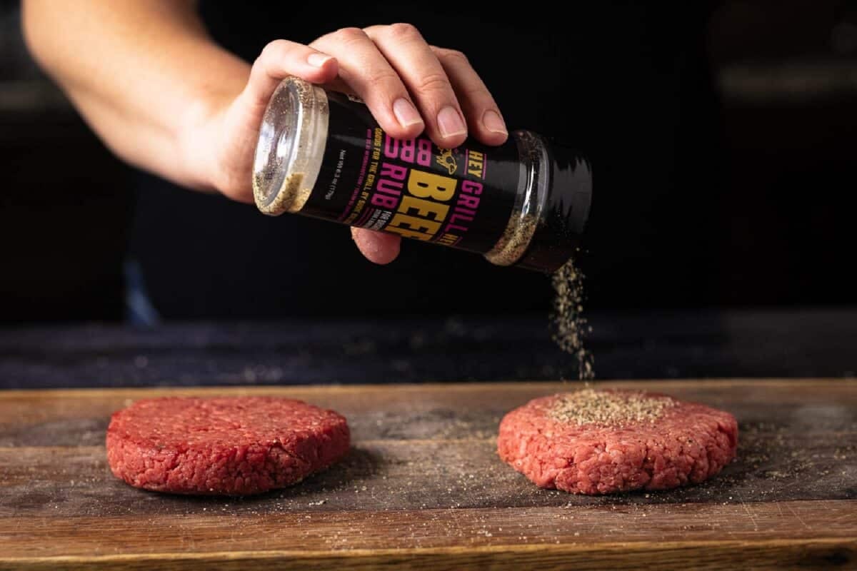 Burger patties being sprinkled with seasoning.