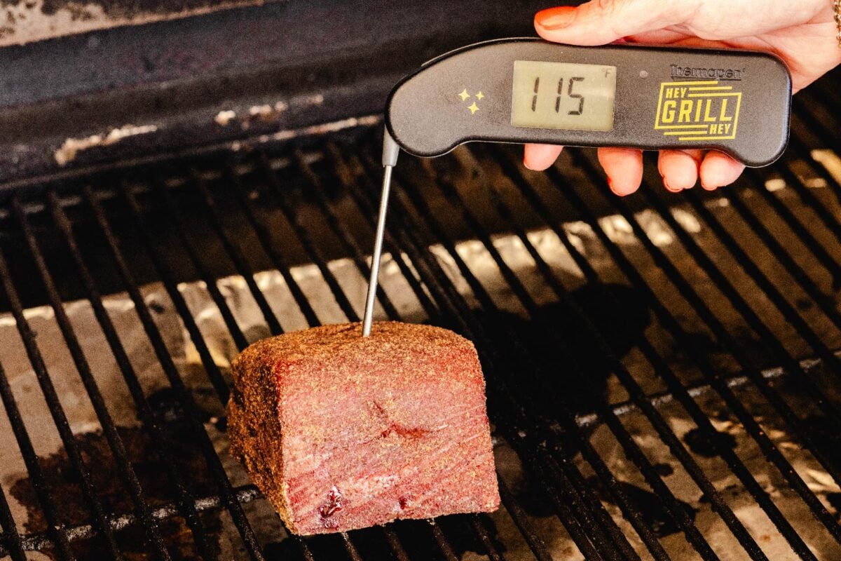 Beef tenderloin on the smoker with a thermometer reading the temperature of 115 degrees F.
