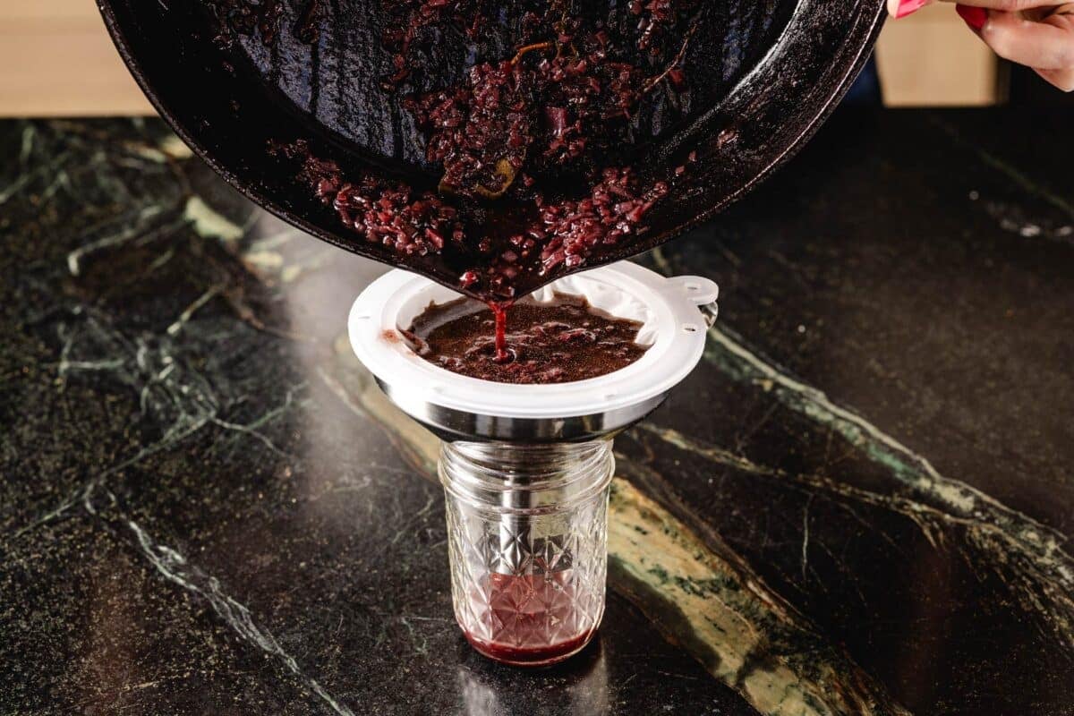 Red wine sauce being strained from a skillet into a jar.