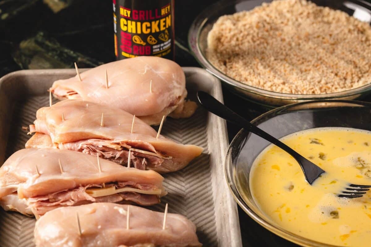 Chicken breasts on baking sheet next to bowls of wet and dry dredges.